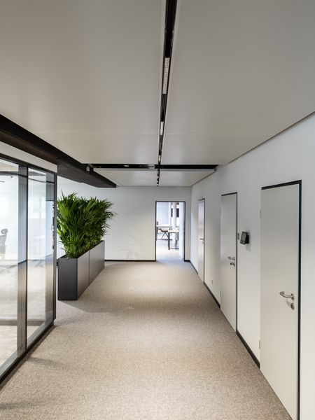 Minimalistische Flurbeleuchtung mittels schwarzem 48V-Schienensystem: Die deckenbündig installierte Schiene mit linearen Lichteinsätzen betont die moderne Architektur des Bürokorridors.