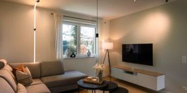 Minimalistisches Wohnzimmer mit einem dunkelgrünen Ecksofa, Zierkissen, einem weißen Couchtisch und sanfter 48-V-Schienenbeleuchtung.