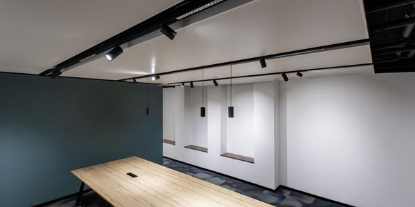 Moderner Konferenzraum mit einem langen Holztisch, weißen Wänden, einer grünen Akzentwand und Decken-Schienenbeleuchtung.