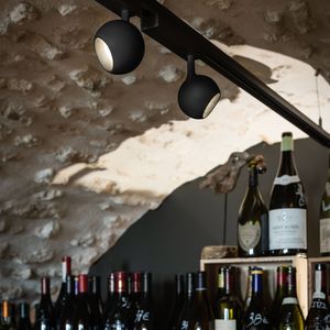 Wine bottles on a stone shelf under LIGHT EYE track lighting, with a rustic stone wall in the background.