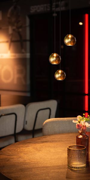 Cozy interior with DYSKO pendant lights, a round table, a small vase with flowers, and bar stools in the background.