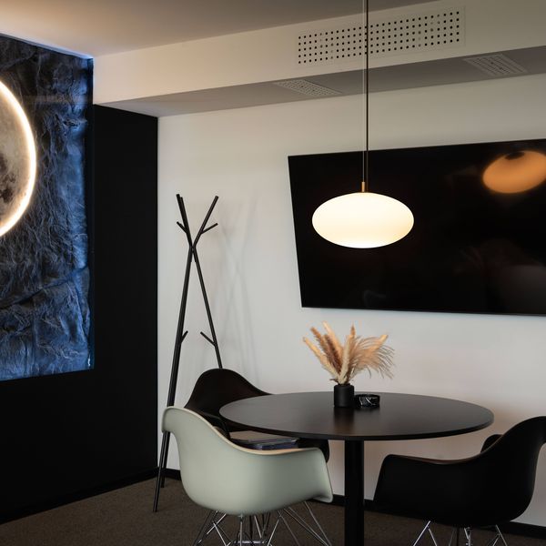 Modern room with a round table and OLYPSO pendant luminaire, two chairs, a wall-mounted TV, a coat rack, and a moon-themed wall light.