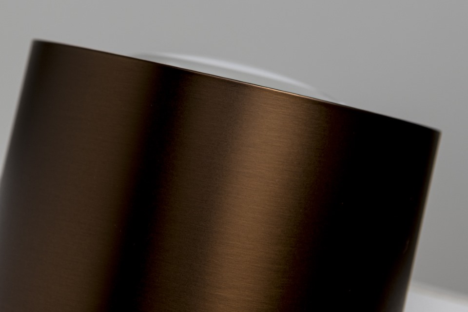 Close-up of a sleek, cylindrical metallic object with a smooth, dark brown finish and a reflective surface against a neutral background.