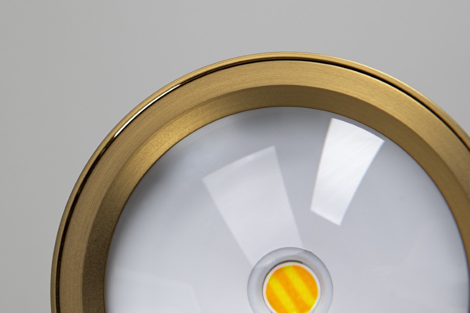 Close-up of a modern circular ceiling light with a gold rim and reflective white surface, featuring a small yellow center detail.