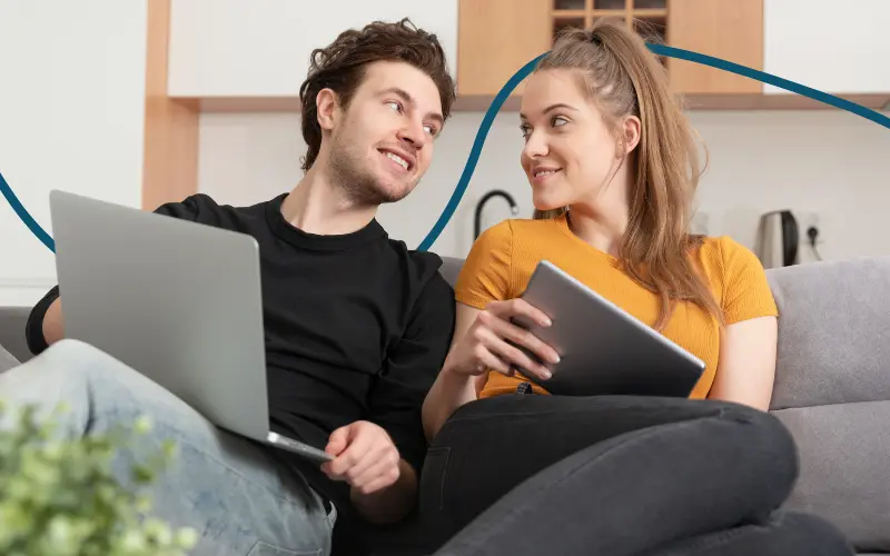 Ungt par sidder i sofaen med deres computer og Ipad