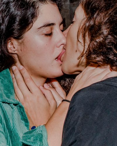Two people kissing closely, with one wearing a green top and the other a black shirt, hands gently touching each other's necks.