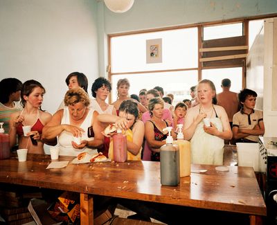 A group of people line up at a counter with food and condiments, eagerly preparing and enjoying snacks.