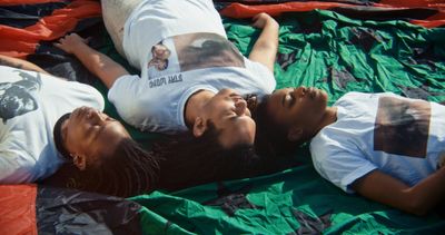 Three people lying on a colorful fabric, wearing white T-shirts with printed images, eyes closed, and facing upward.
