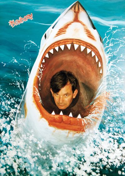 Man poses inside a large shark's open mouth, surrounded by painted ocean waves, with the word "Benidorm" in the corner.