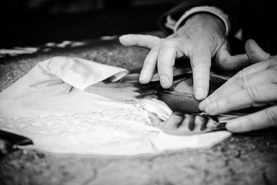 Hands gently touching a textured surface with a printed image of a white shirt, possibly engaging in a tactile exploration or art activity. Black and white photo.