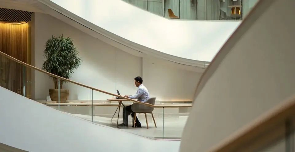 A person working alone at a desk on a curved, light-filled atrium