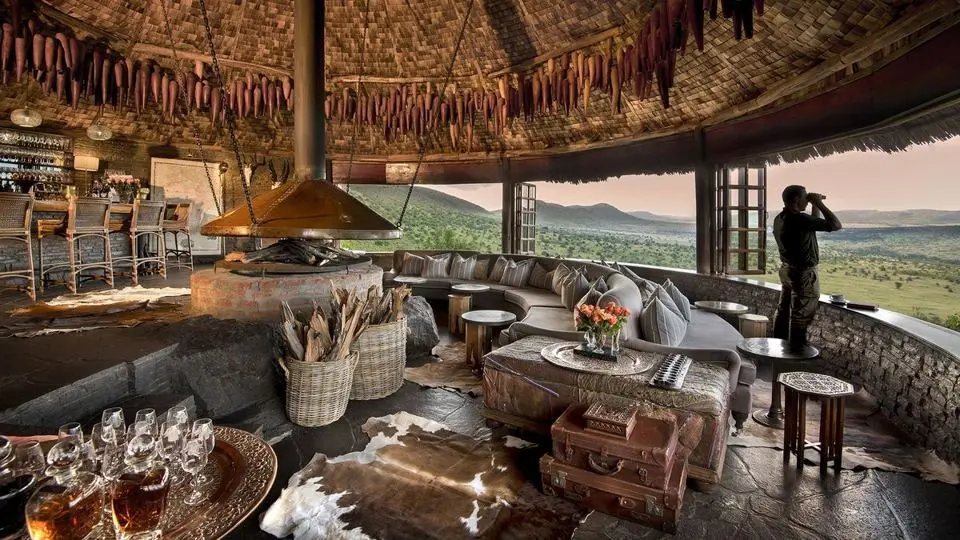 A safari lodge lounge with a fire pit, looking out over open grassland
