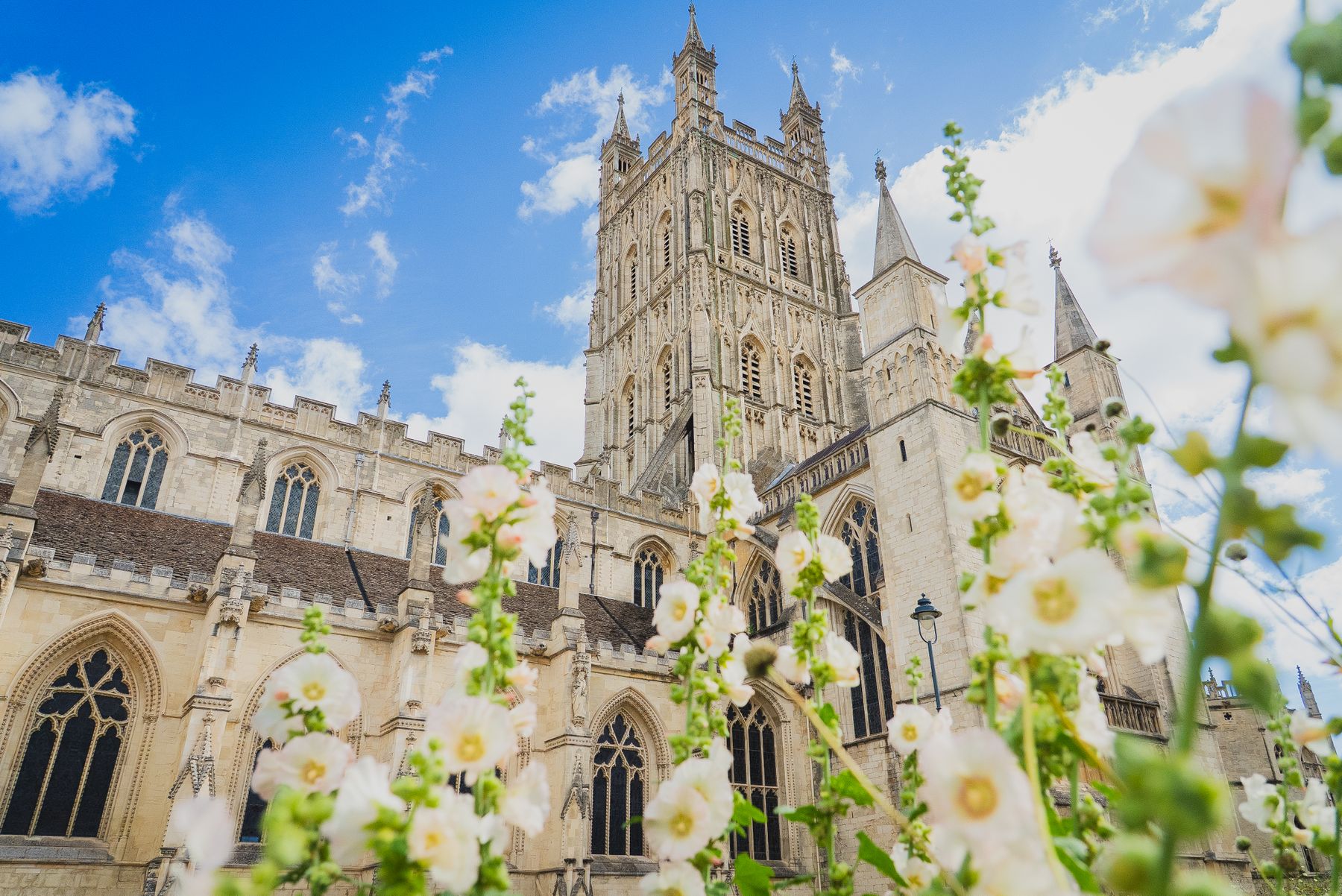 Gloucester Cathedral under a blue sky with flowers in front