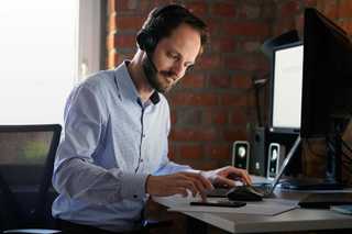 Symbolbild, ein Mann an einem Schreibtisch, der mit einem Headset arbeitet