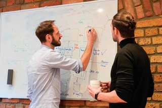 Symbolbild, zwei Männer vor einer Tafel, die Leistungen besprechen