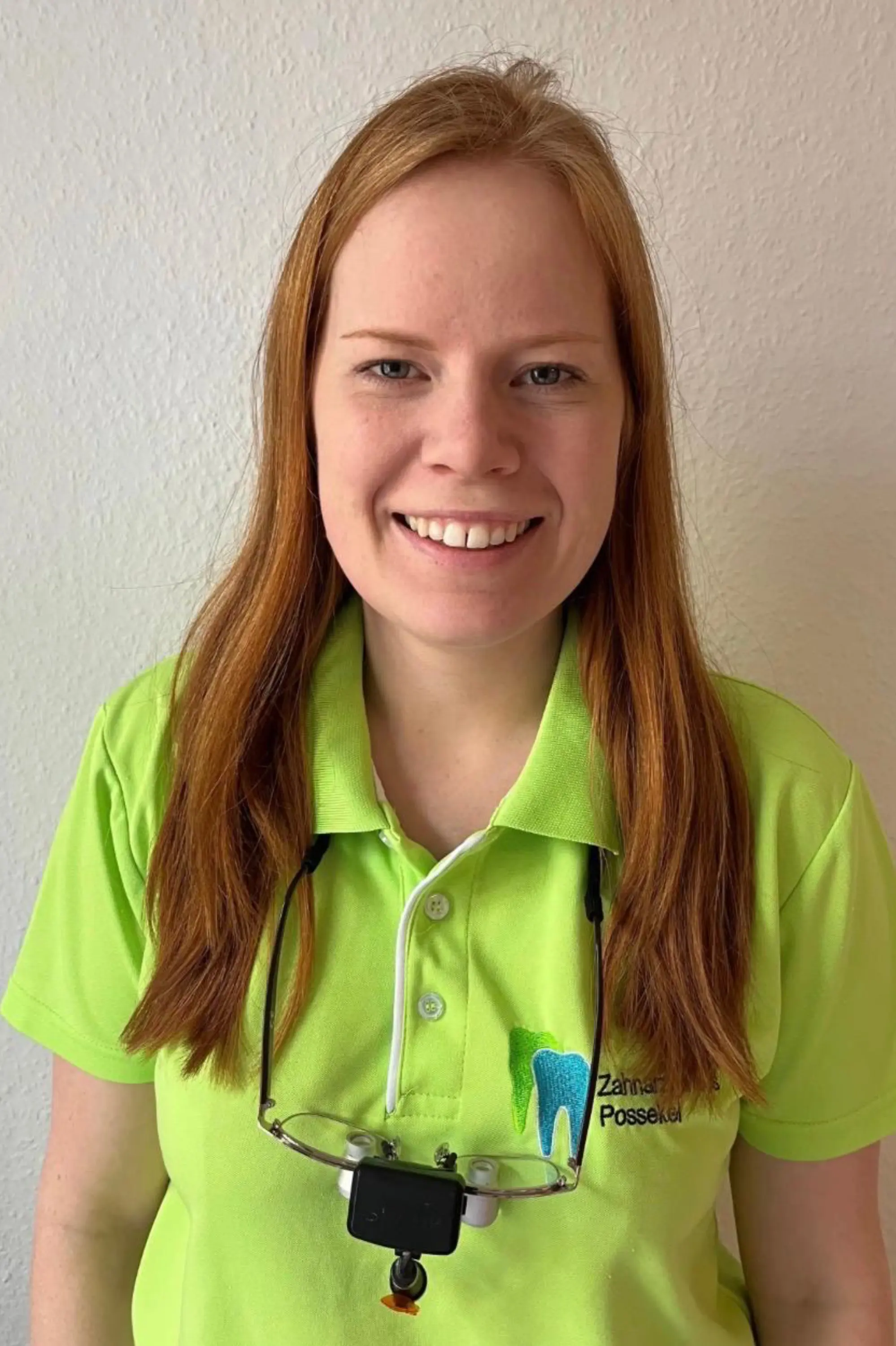 Woman smiling in a green polo shirt with a dental logo, wearing dental loupes.