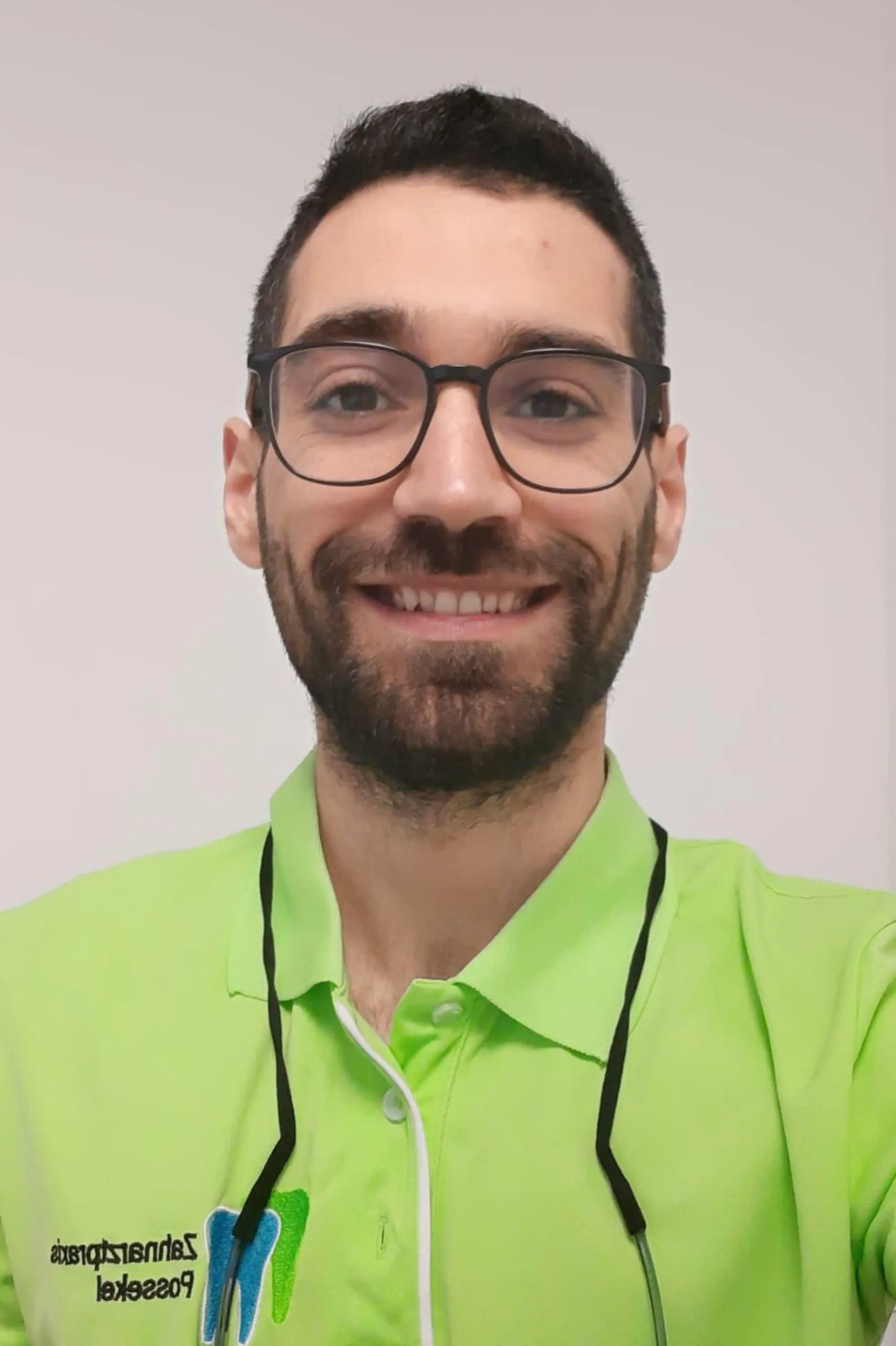 A man with glasses and a beard smiling, wearing a bright green polo shirt with a black lanyard.