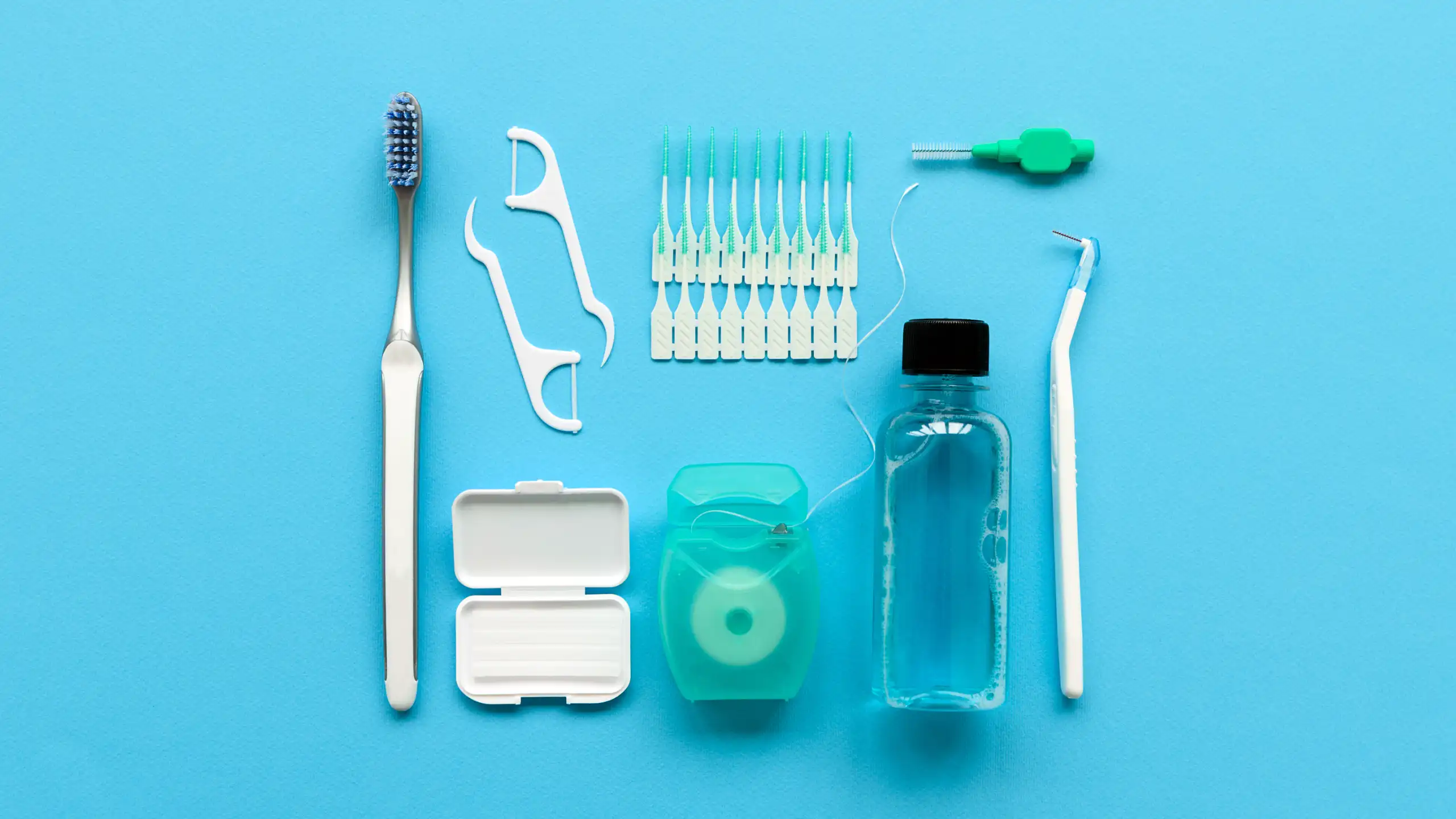 Dental care items on a blue background, including a toothbrush, floss picks, interdental brushes, dental floss, mouthwash, and a dental scaler.