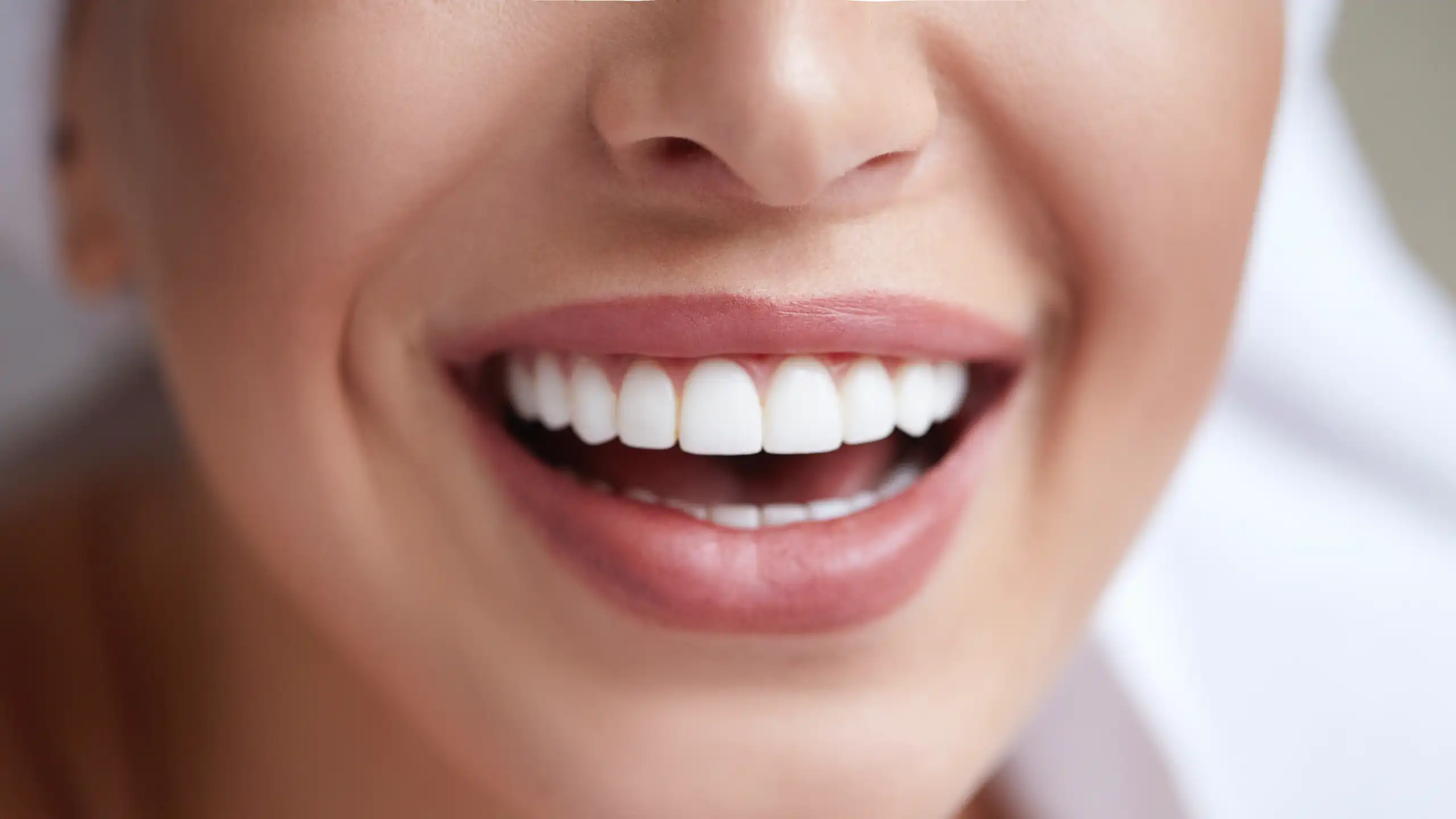 Close-up of a person smiling, showing bright white teeth and slightly parted lips, with smooth skin and a hint of a towel in the background.