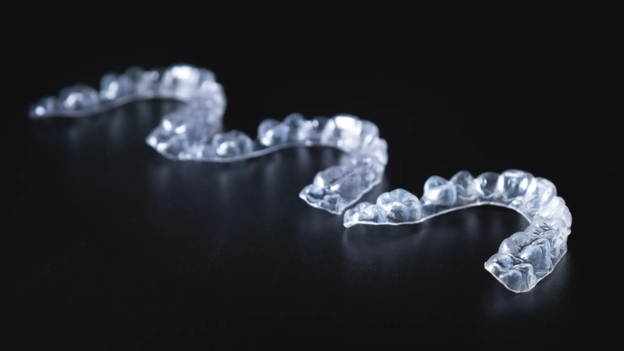 Close-up of clear aligners on a dark surface, showing detailed impressions of teeth.