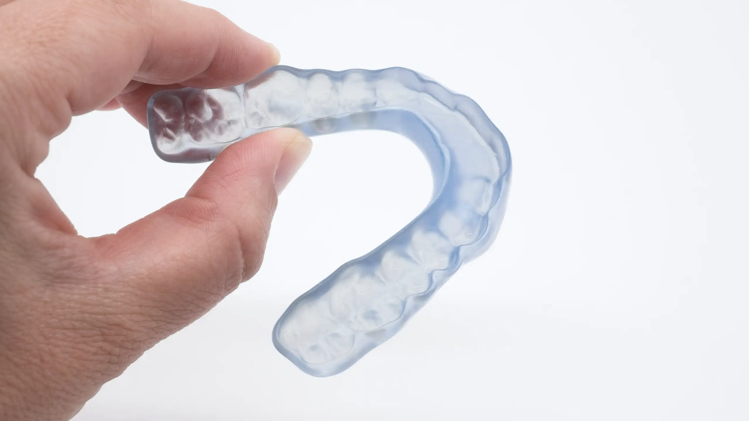 Hand holding a translucent U-shaped dental night guard (mouthguard) against a white background.