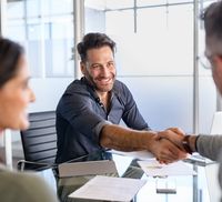 A mortgage broker shaking hands with clients who are refinancing with home loan documents on the table