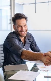A mortgage broker shaking hands with clients who are refinancing with home loan documents on the table