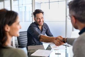 A mortgage broker shaking hands with clients who are refinancing with home loan documents on the table