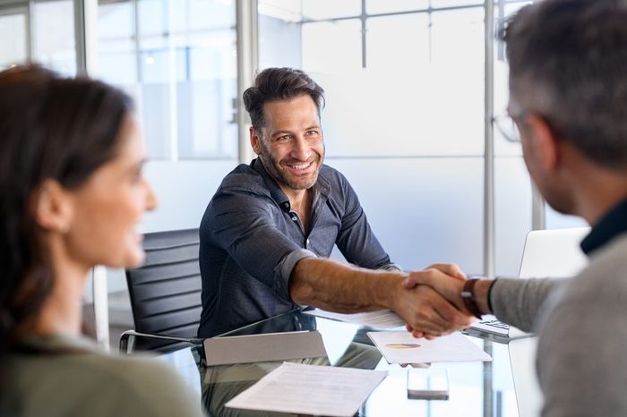 A mortgage broker shaking hands with clients who are refinancing with home loan documents on the table