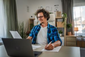 A man on his laptop looking at smsf loans in his home filling out paperwork