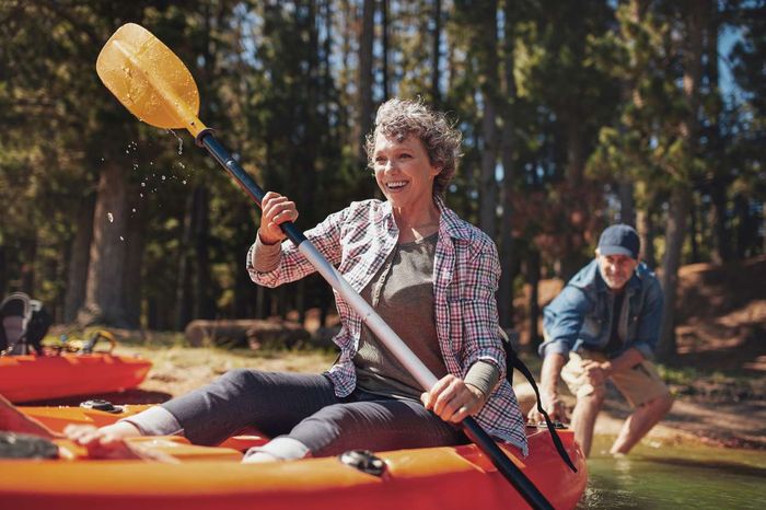 A mature lady kayaking on a lake with her partner in the background