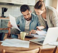 A couple looking at mortgage documents on their kitchen table as they consider to refinance