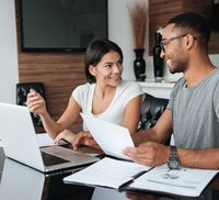 A couple looking at refinance home loan documents in front of a laptop in their living room