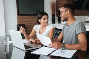 A couple looking at refinance home loan documents in front of a laptop in their living room