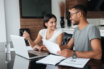 A couple looking at refinance home loan documents in front of a laptop in their living room