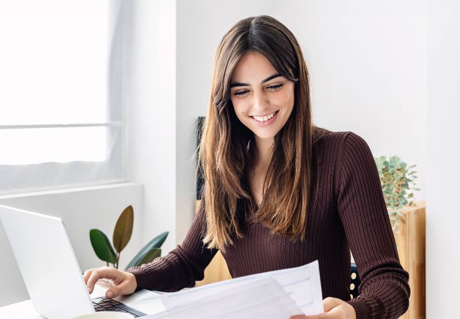 A young lady looking over her finances at a computer desk smiling