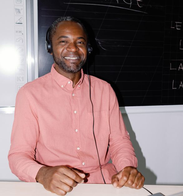Smiling man in a pink shirt and headphones sitting in front of a laptop