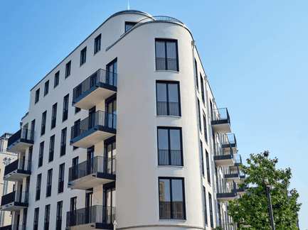 Modernes Mehrfamilienhaus mit Balkonen und abgerundeter Gebäudeecke vor blauem Himmel.