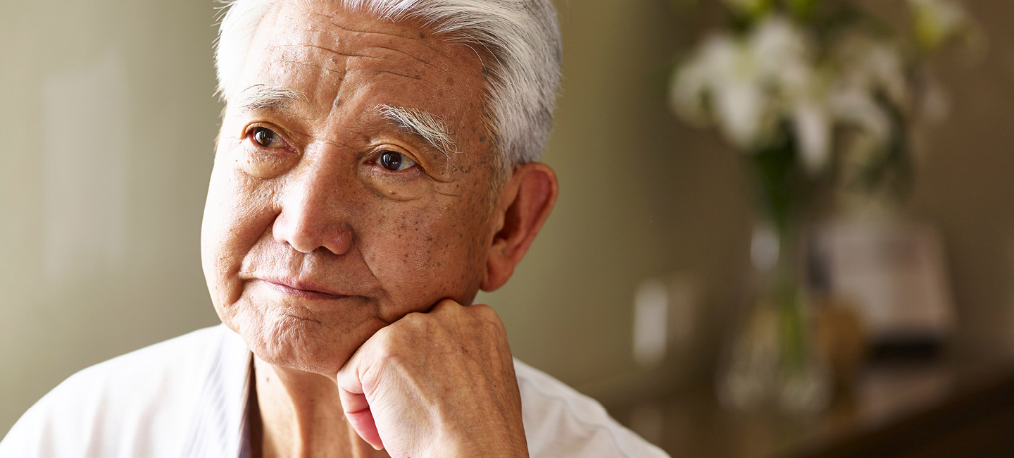 Image of an older asian man resting his chin on his left hand