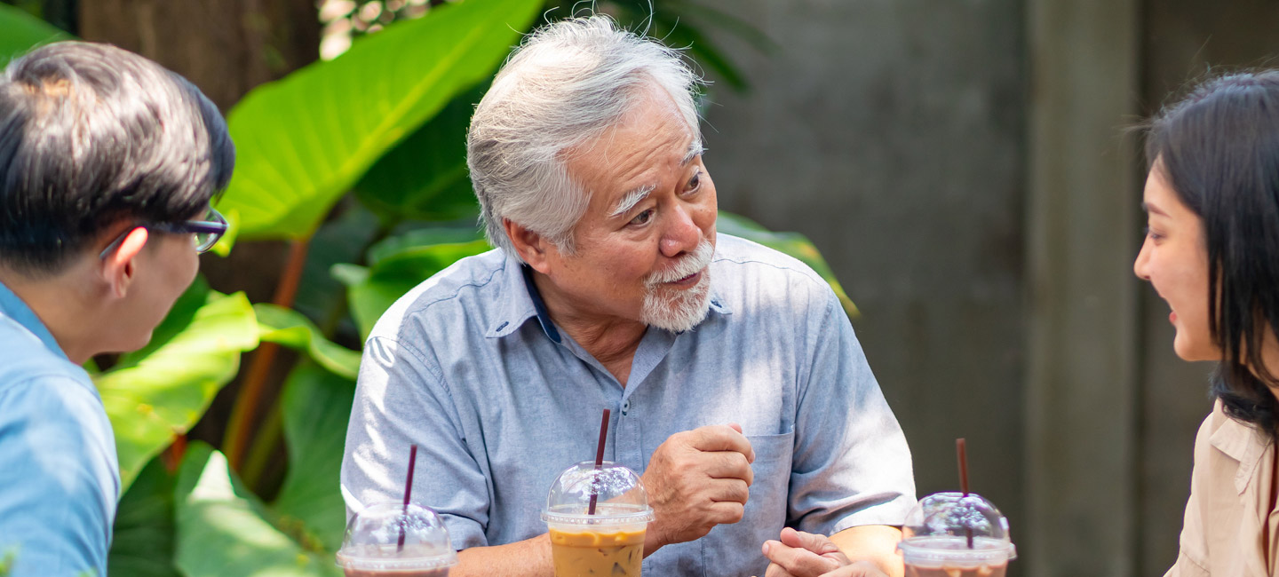 Image of an older asian man sitting outside and talking with friends