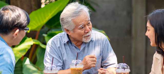 Hình ảnh một người đàn ông châu Á lớn tuổi ngồi bên ngoài và nói chuyện với bạn bè