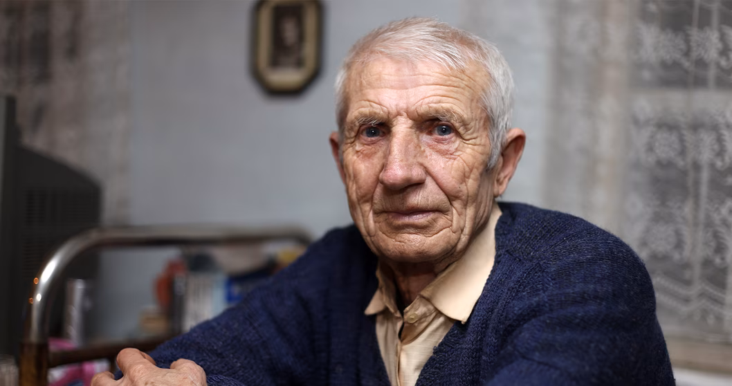 Image of an older man who is sitting down in his bedroom