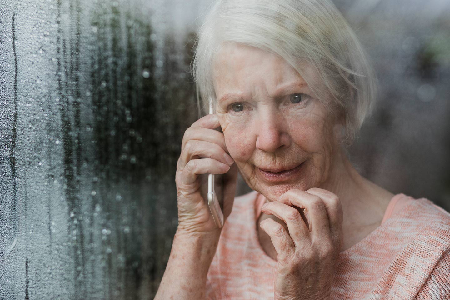 Photo of woman on a mobile phone looking through a rainy window