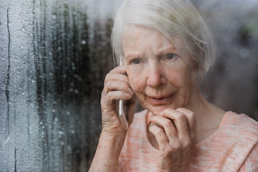 Photo of woman on a mobile phone looking through a rainy window