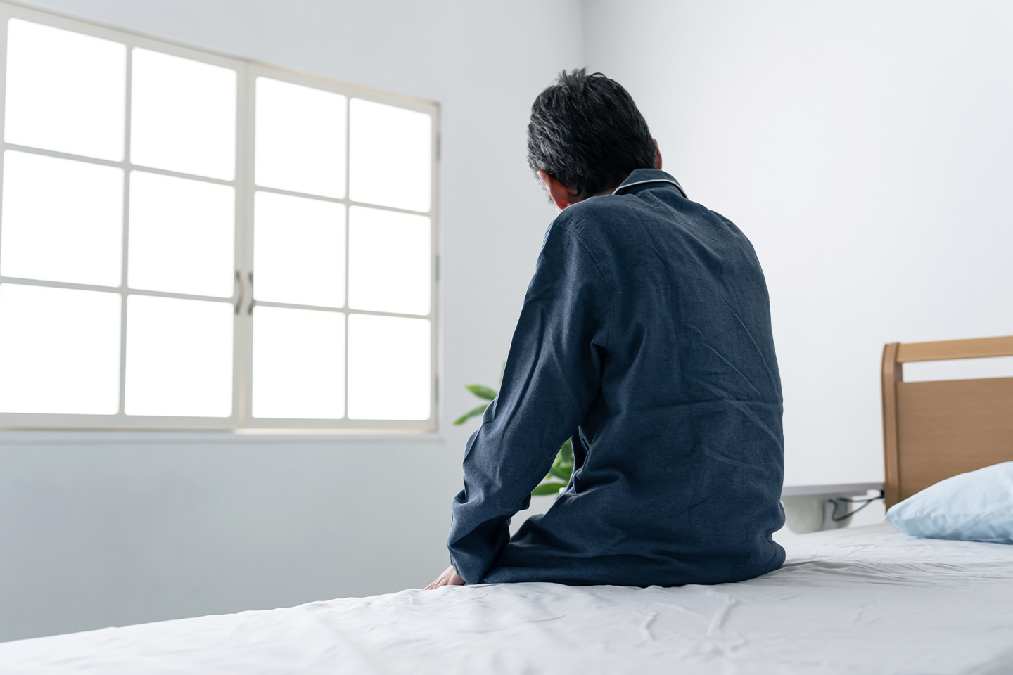 Photo of man with his back to us sitting on the edge of a bed