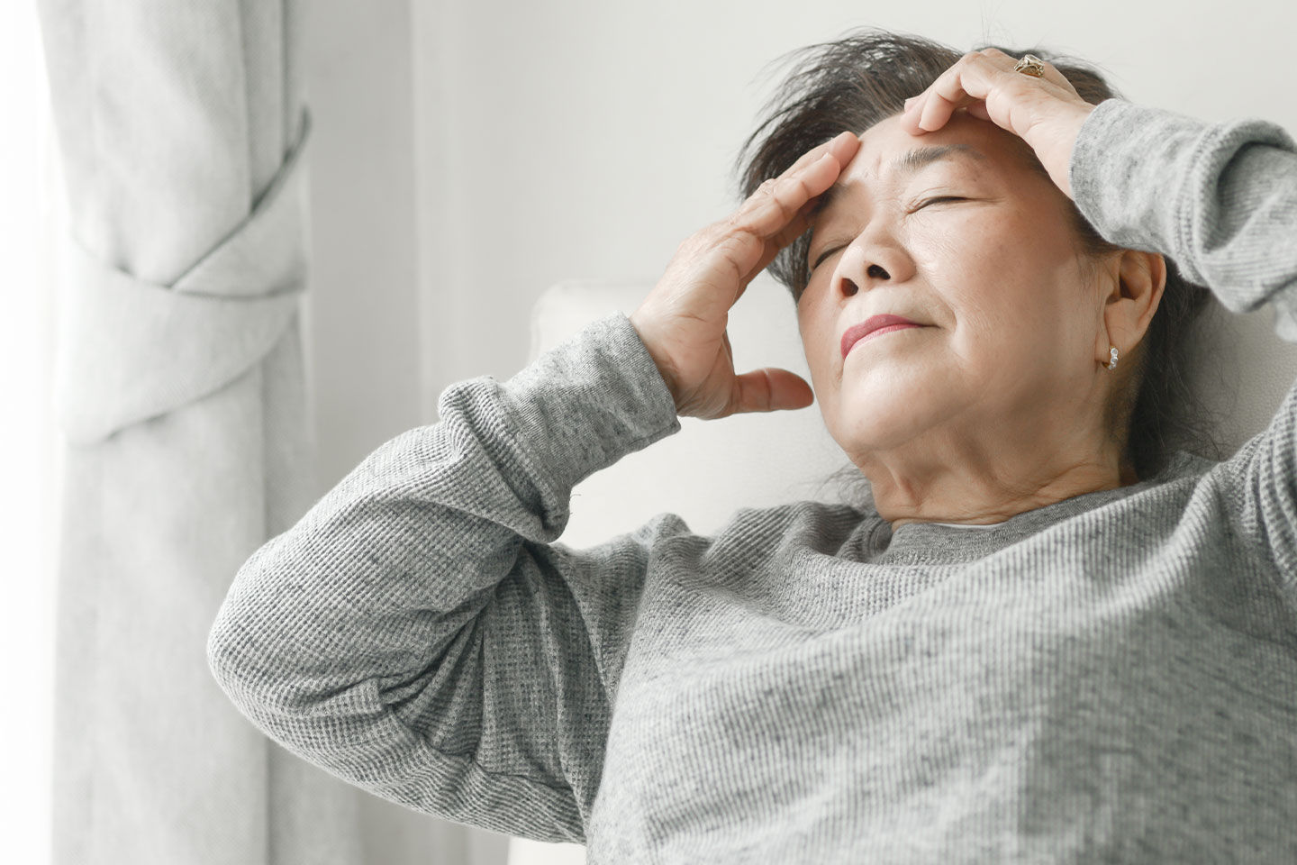 Photo of woman in grey sweatshirt massaging her forehead