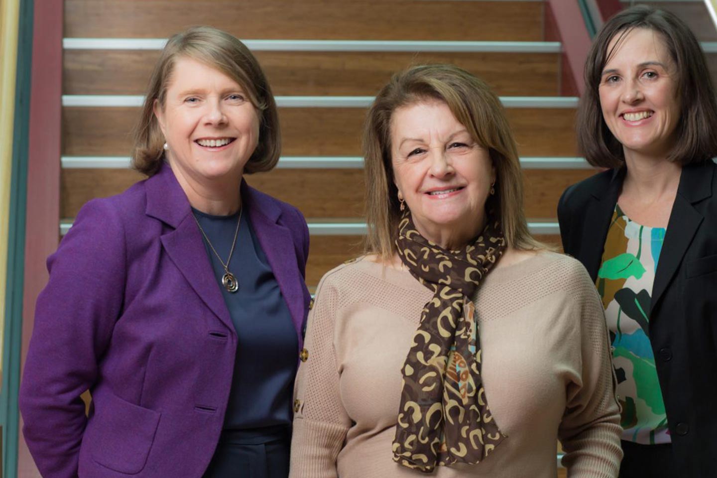 Photo of three women smiling at us in front of a staircase