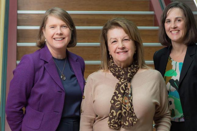 Photo of three women smiling at us in front of a staircase