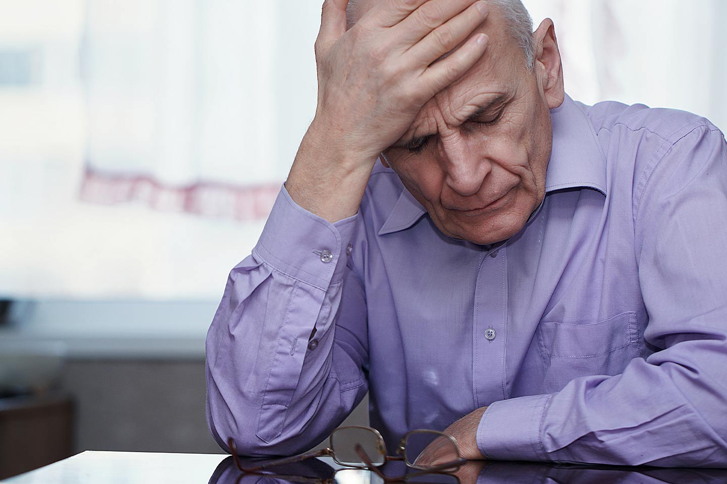 Photo of a man in a pale lavender shirt with his head in his hand