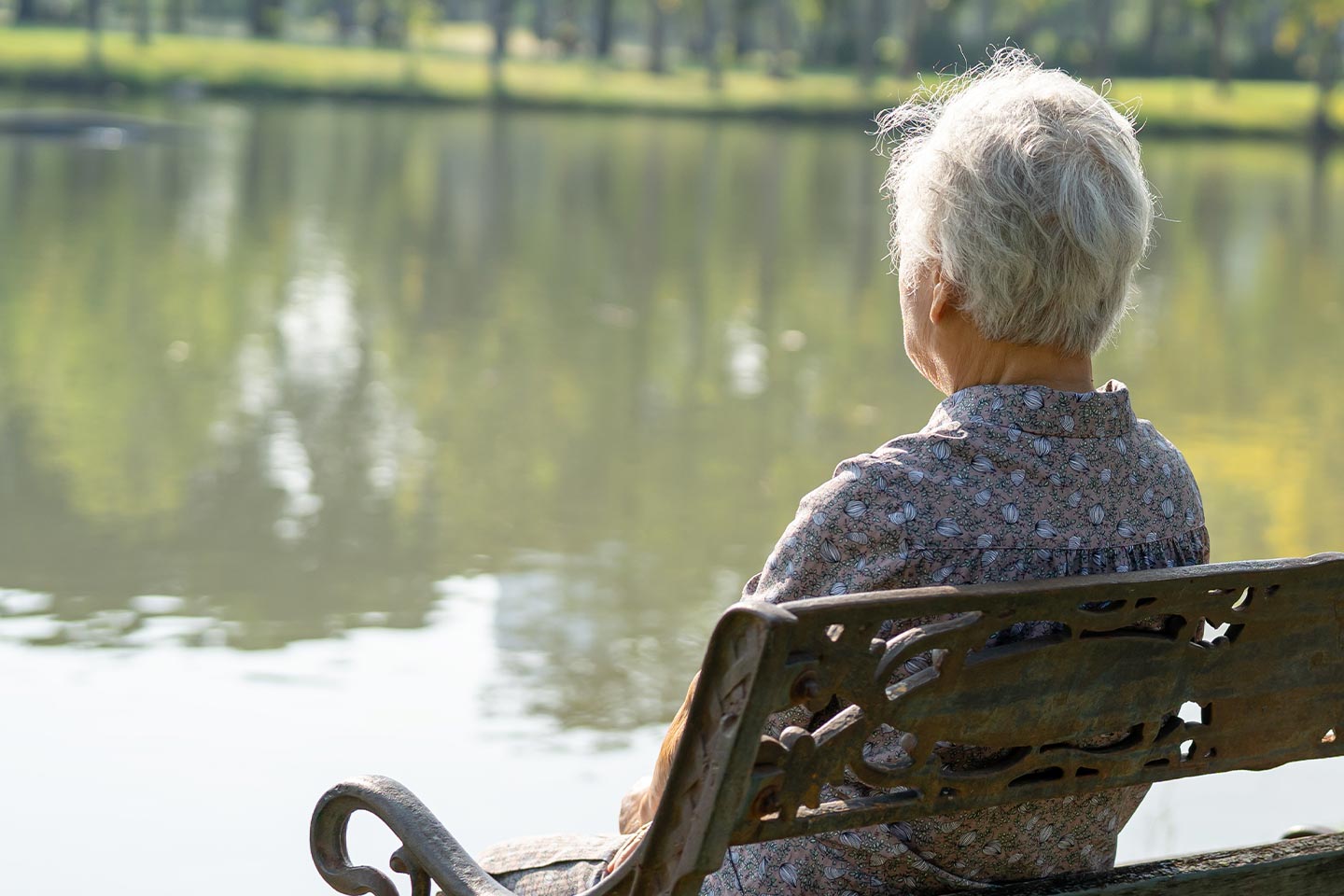 Photo of a person sitting on a park bench looking at a pond